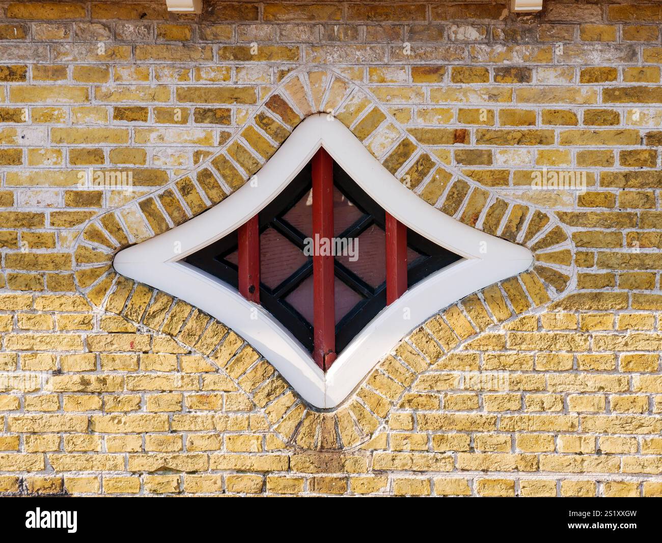 Diamantförmiges Fenster mit schwarzen und dunkelroten Mantinen, in weißem Holzrahmen, in Ziegelfassade eines alten Hauses in Hindeloopen, Friesland, Niederlande Stockfoto