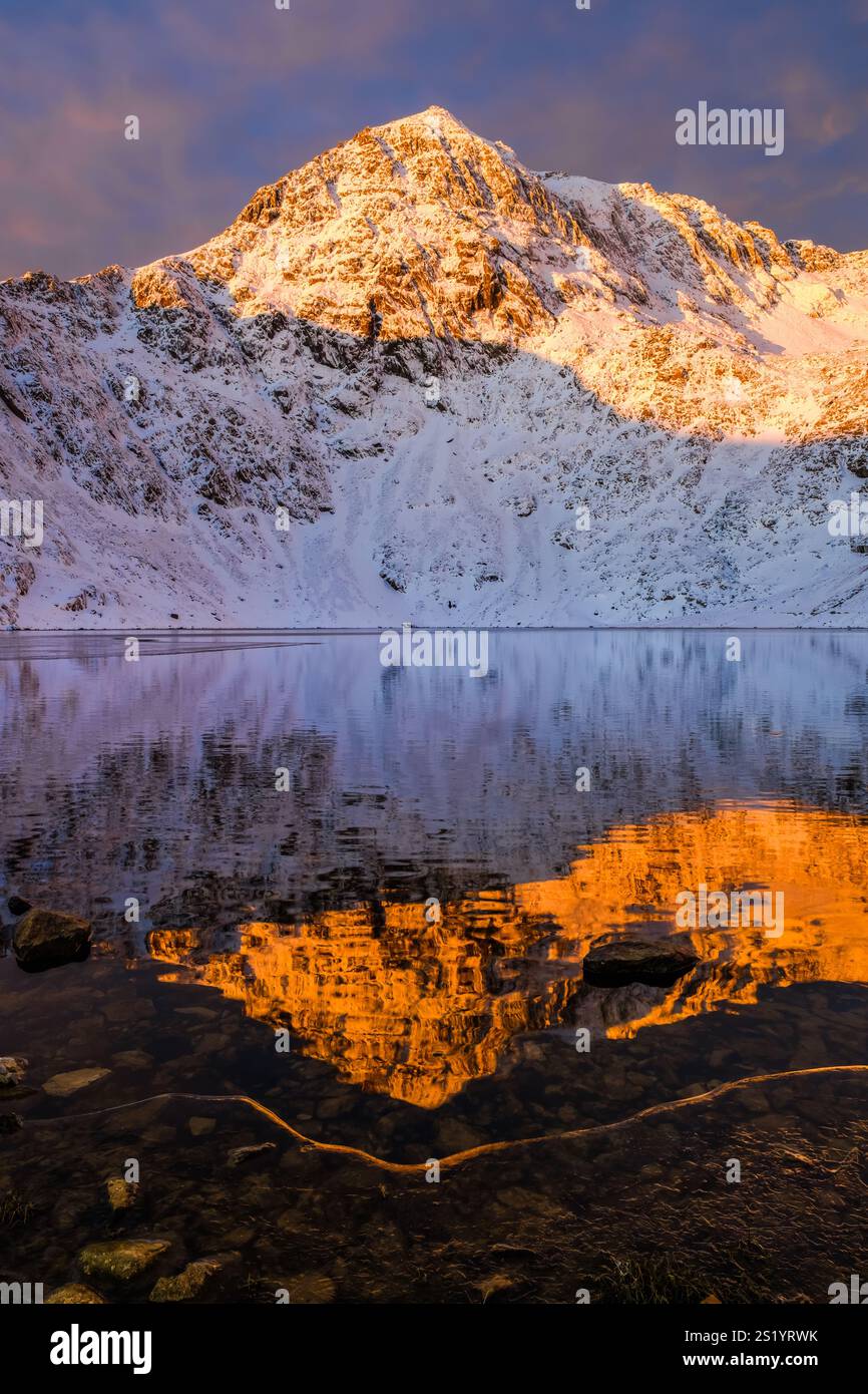 Ein Blick auf den Wintersonnenaufgang von Yr Wyddfa, oder Snowdon, spiegelt sich im eisigen Wasser eines teilweise gefrorenen Glaslyn unterhalb, Eryri (Snowdonia National Park), Wales Stockfoto