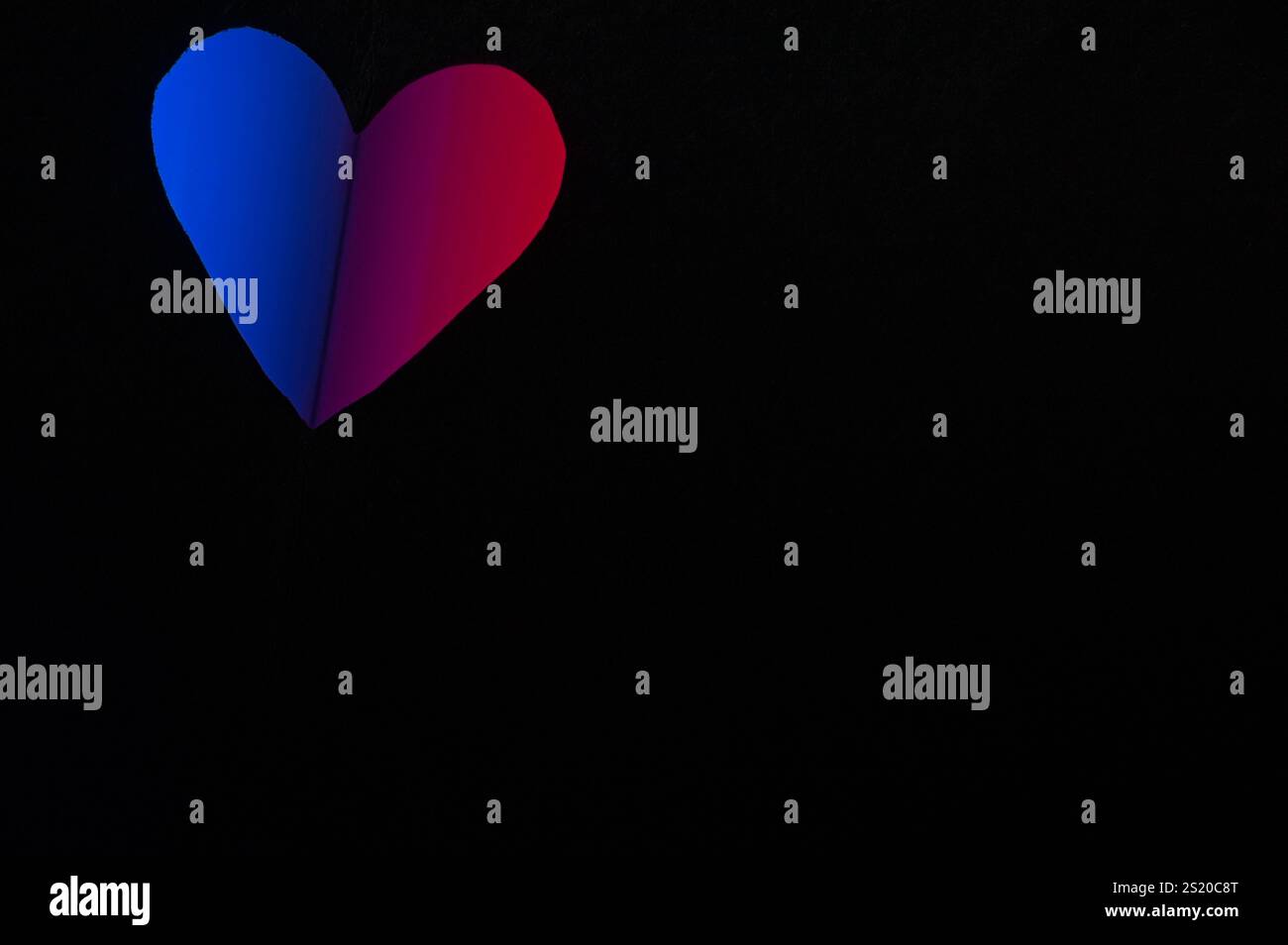 Herzausschnitt aus schwarzem Papier mit durchscheinendem rotem und blauem Licht Stockfoto