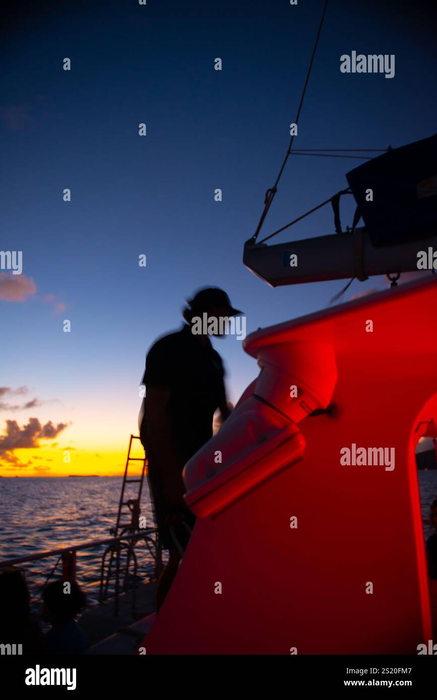 Eine Silhouette eines Seemanns vor einem glühenden Himmel bei Sonnenuntergang, hervorgehoben durch das kühne Karmesinrot an Bord, Die Eine ruhige, aber dramatische Szene beleuchtet, die das Essen festhält Stockfoto