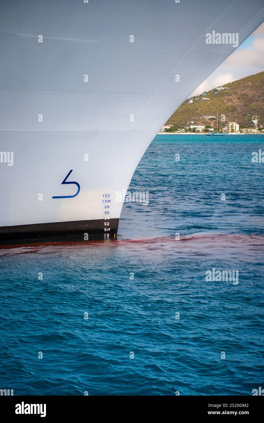 Eine minimalistische Nahaufnahme eines Kreuzfahrtbogens mit seinem schlanken Design und den präzisen Wasserlinien vor dem leuchtenden Blau eines ruhigen Hafens Stockfoto