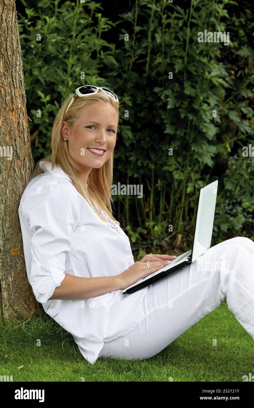 Eine junge Frau sitzt mit einem Laptop im Garten und surft im Internet. WLAN im Park. Österreich Stockfoto