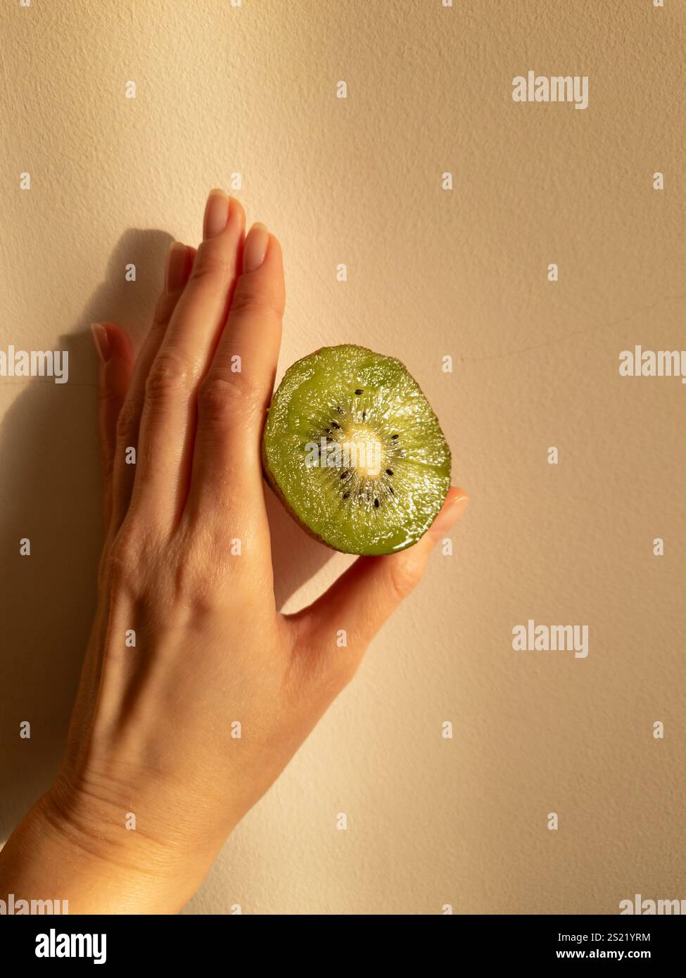 Die Hand hält eine offene Kiwi in einem weichen, warmen Licht - Smartphone-aufgenommenes Stockfoto