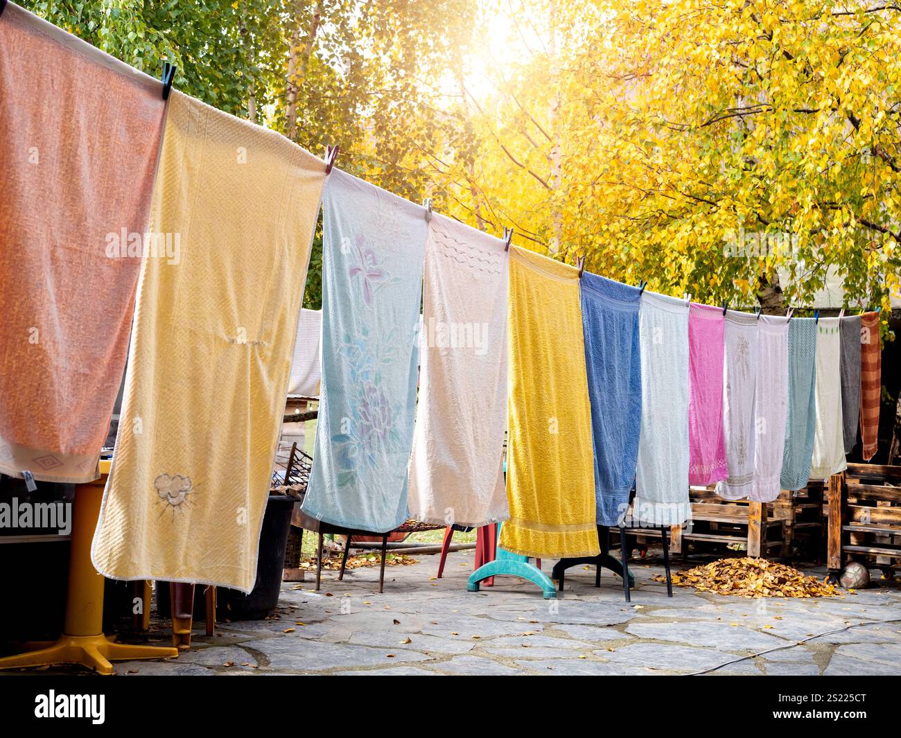 Bunte Handtücher hängen Wäsche an der Wäscheleine im Garten im Herbst. Wäscheleine mit frisch gewaschener mehrfarbiger Kleidung im Freien A Stockfoto