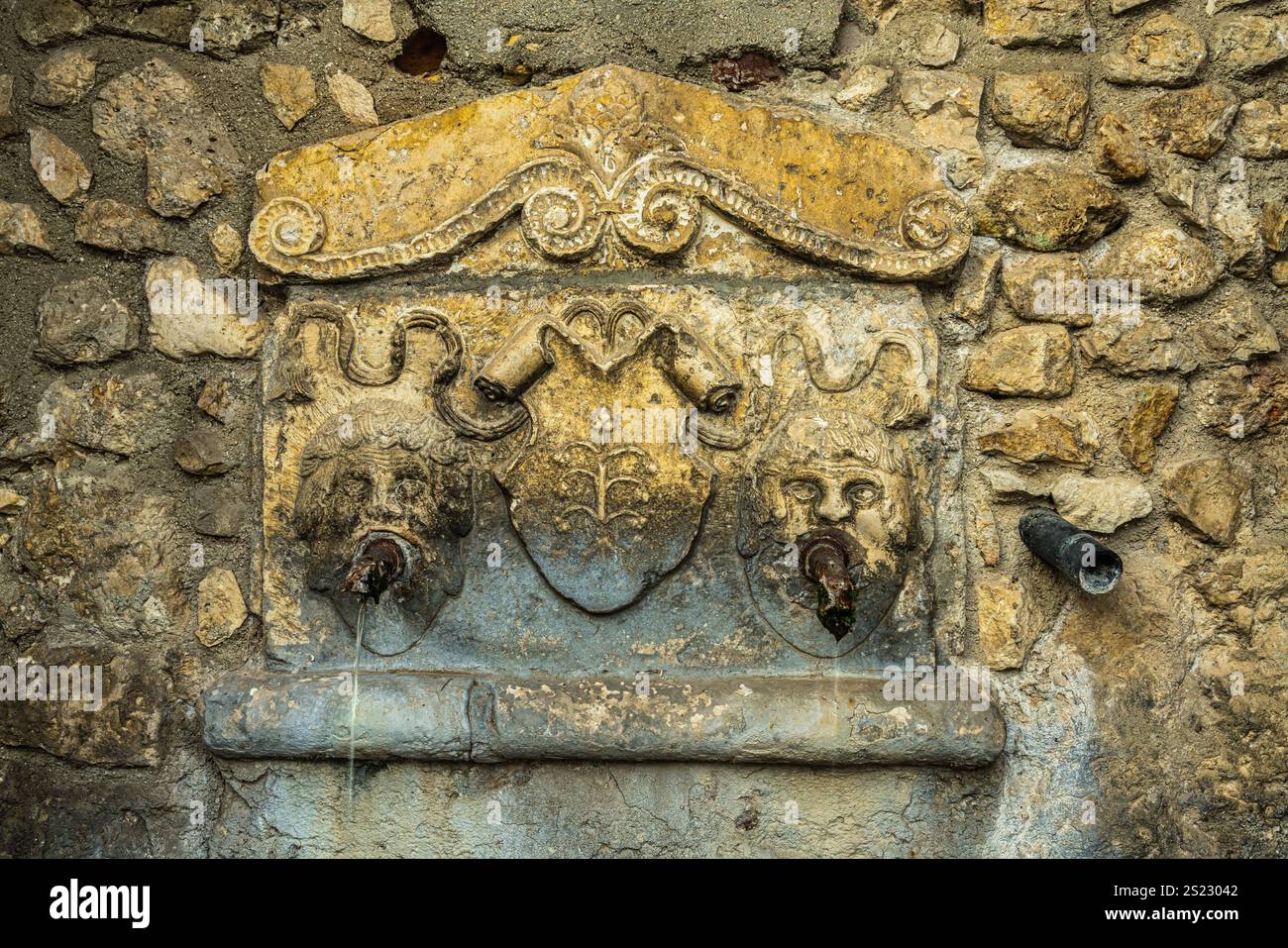 Detail der Nische im öffentlichen Brunnen mit zwei dekorativen Masken im historischen Zentrum des mittelalterlichen Dorfes Acciano. Acciano, Abruzzen Stockfoto