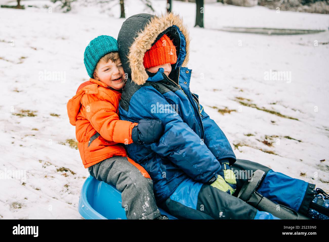 Geschwister, die sich auf einem Schlitten lachen, während verschneite Winterspaß Stockfoto