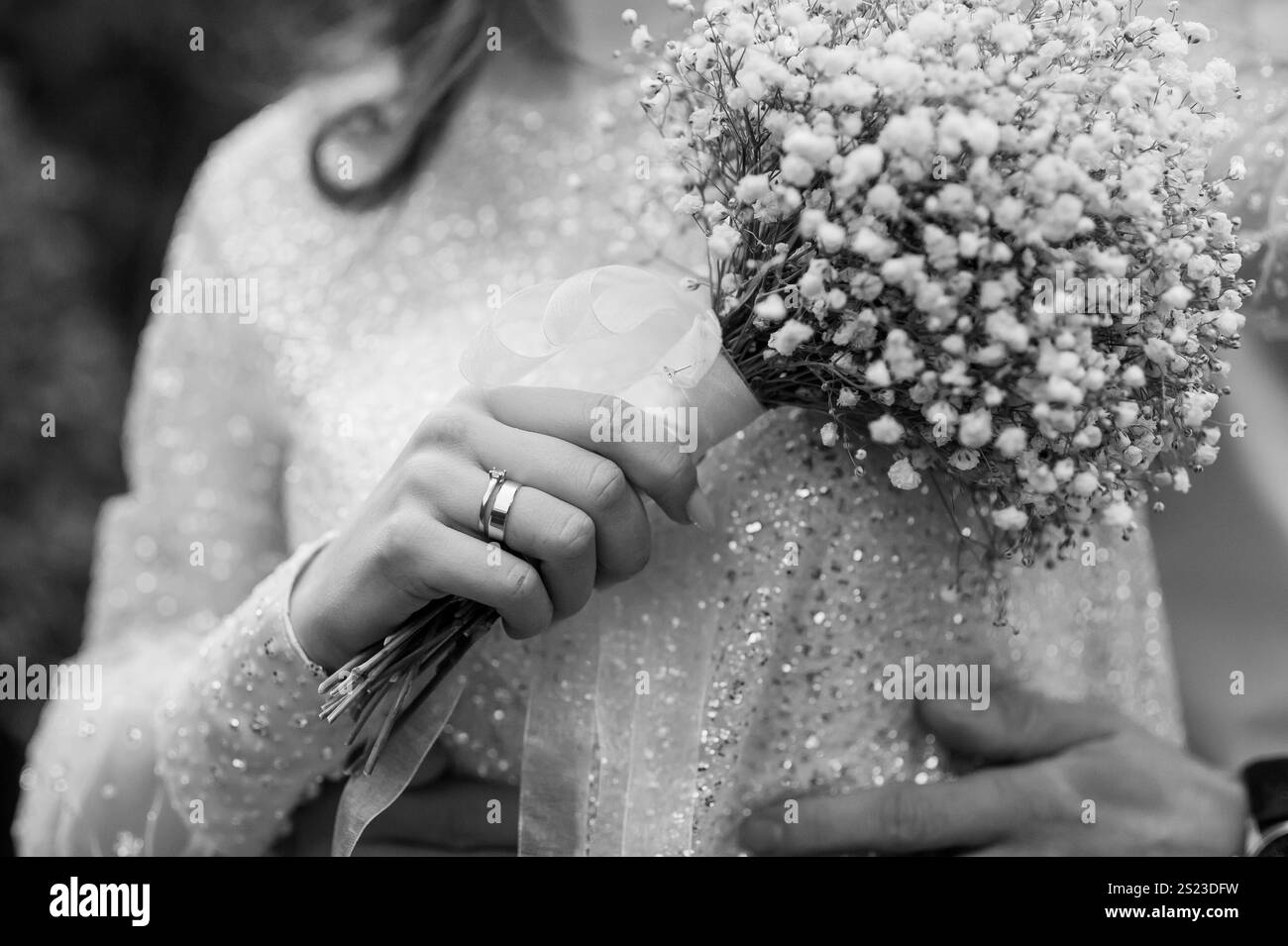 Elegante Braut mit zartem Blumenstrauß und Bräutigam-Umarmung in Schwarz und weiß. Stockfoto