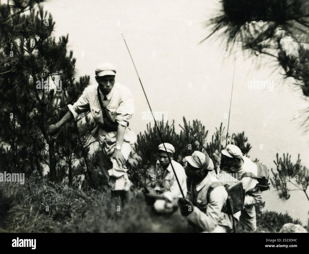 Soldaten, die bei Sonnenaufgang in einem bewaldeten Gebiet einen Hügel besteigen, gekleidet in leichte Uniformen und ausgerüstet für eine Übung: 1950er Jahre PLA Field Radio Operation: Ein Blick in die chinesische Militärkommunikationsgeschichte. Stockfoto Soldaten, die bei Sonnenaufgang in einem bewaldeten Gebiet einen Hügel besteigen, gekleidet in leichte Uniformen und ausgerüstet für eine Übung: 1950er Jahre PLA Field Radio Operation: Ein Blick in die chinesische Militärkommunikationsgeschichte. Stockfoto