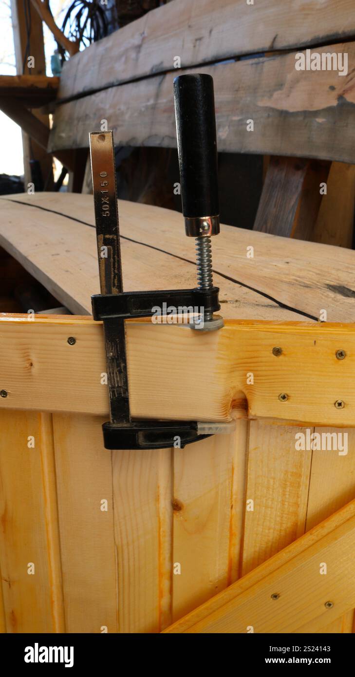 Verkleben der Bauteile einer kleinen Holztür mit einer Klammer, Verbinden und Klemmen der Bretter in einer hausgemachten Scheunentür Stockfoto