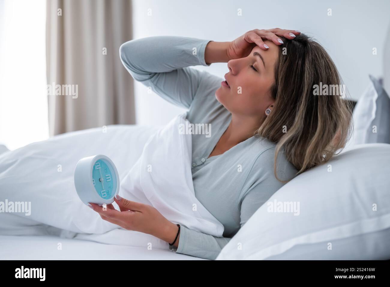 Die Frau wacht morgens auf und hält die Uhr. Stockfoto