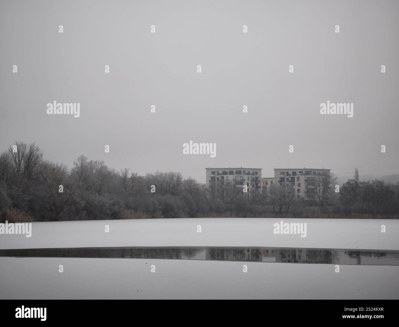 Prag, Tschechische republik - 27. Dezember 2024: Schneebedeckte Landschaft mit einem gefrorenen Seeteich, der Wohngebäude in prag 9, tschechien, während A reflektiert Stockfoto