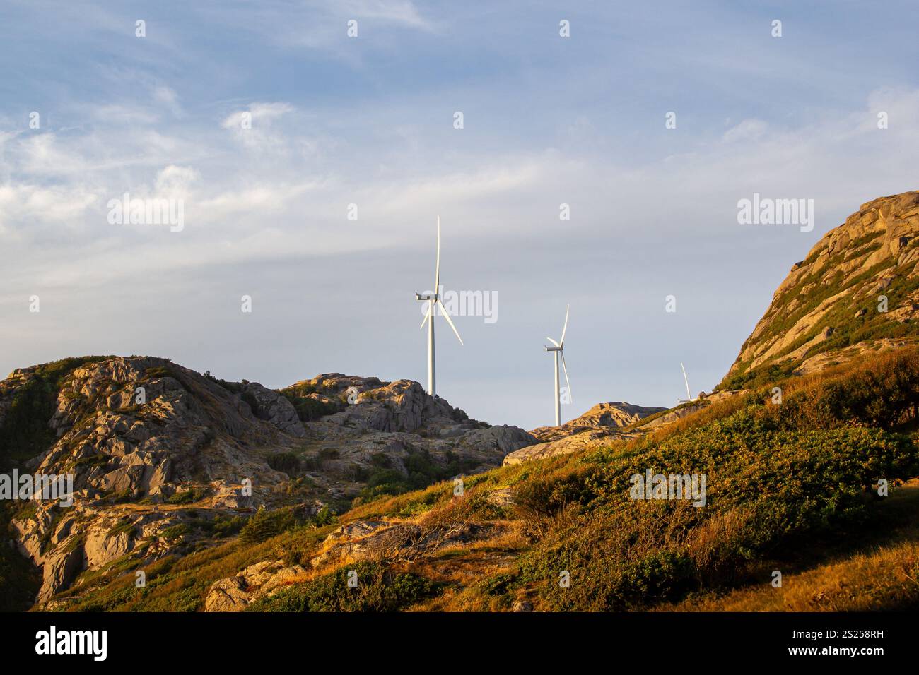 Diese Windturbinen befinden sich auf schroffen Hügeln und nutzen erneuerbare Energie, wenn die Sonne untergeht. Sie strahlen ein warmes Licht über die umliegende felsige Landschaft Stockfoto