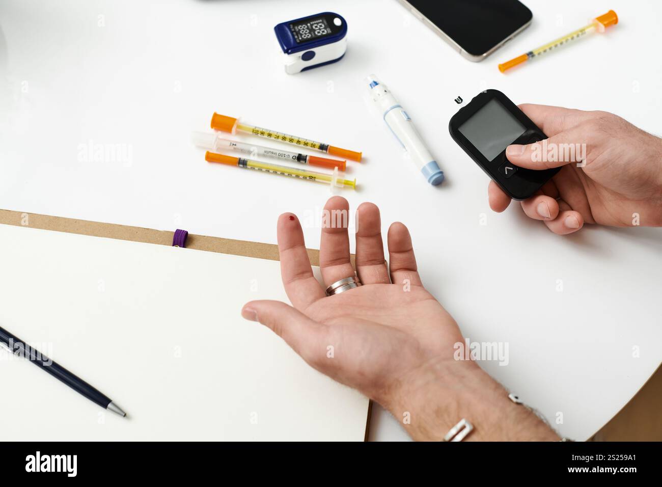 Ein junger Mann kontrolliert den Blutzucker mit einem Messgerät, während er zu Hause von Diabetesmanagement-Tools umgeben ist. Stockfoto