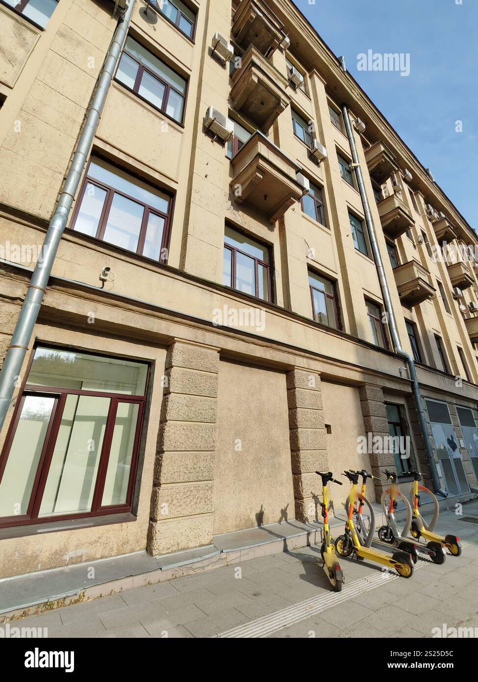 Eine mehrstöckige beigefarbene Fassade mit Balkonen, rechteckigen Fenstern und Gebrauchselementen wie Abflussrohren und Klimaanlagen. Das Foto spiegelt den wider Stockfoto