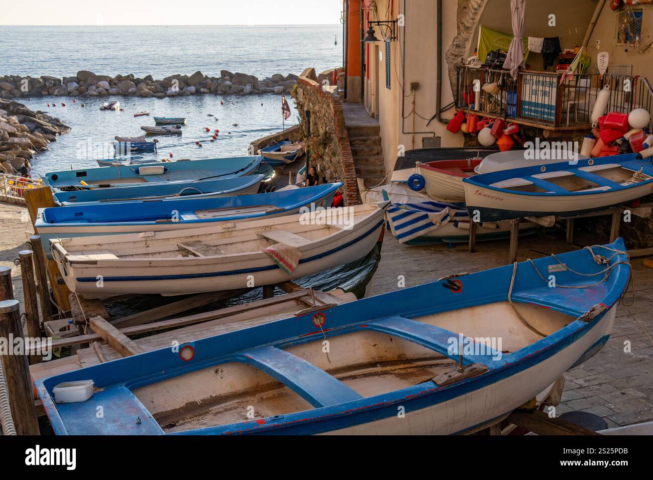 Kleine Ruderboote, die außerhalb des Wassers gelagert werden, mit dem Hafen dahinter in Riomaggiore, Cinque Terre, Italien. Stockfoto