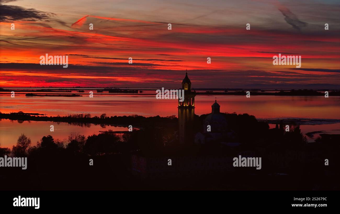 Ein atemberaubender Sonnenuntergang mit wunderschönen Orangetönen, der den Himmel erfüllt und ein warmes Leuchten über die Silhouette eines Schutzgebietes wirft, das friedlich vor ihm steht Stockfoto