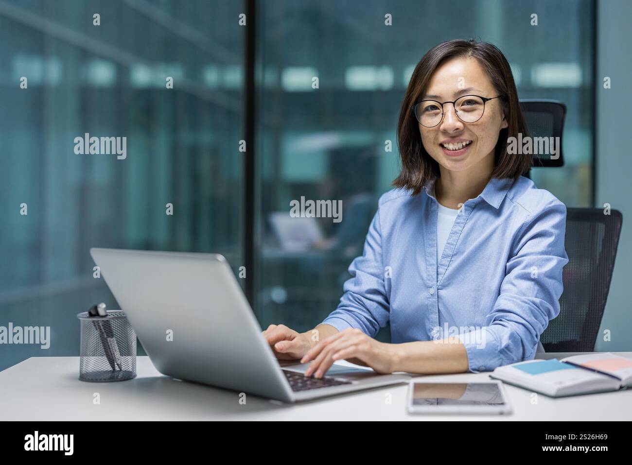 Porträt einer jungen erfolgreichen asiatischen Geschäftsfrau, Büroangestellte lächelnd und in die Kamera schauend, Frau am Arbeitsplatz im Büro, die mit Laptop arbeitet. Stockfoto