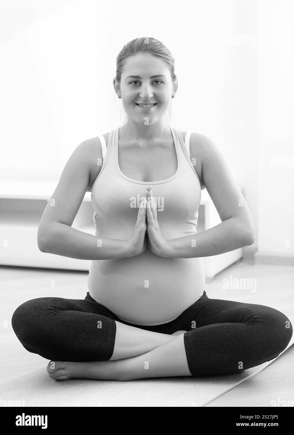 Schwarz-weiß-Foto einer lächelnden schwangeren Frau, die zu Hause Yoga praktiziert Stockfoto