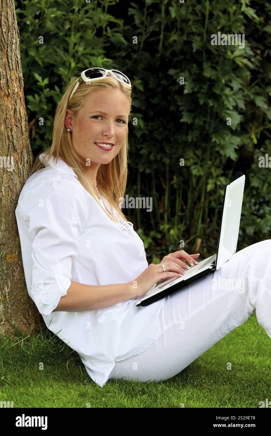 Eine junge Frau sitzt mit einem Laptop im Garten und surft im Internet. WLAN im Park. Österreich Stockfoto
