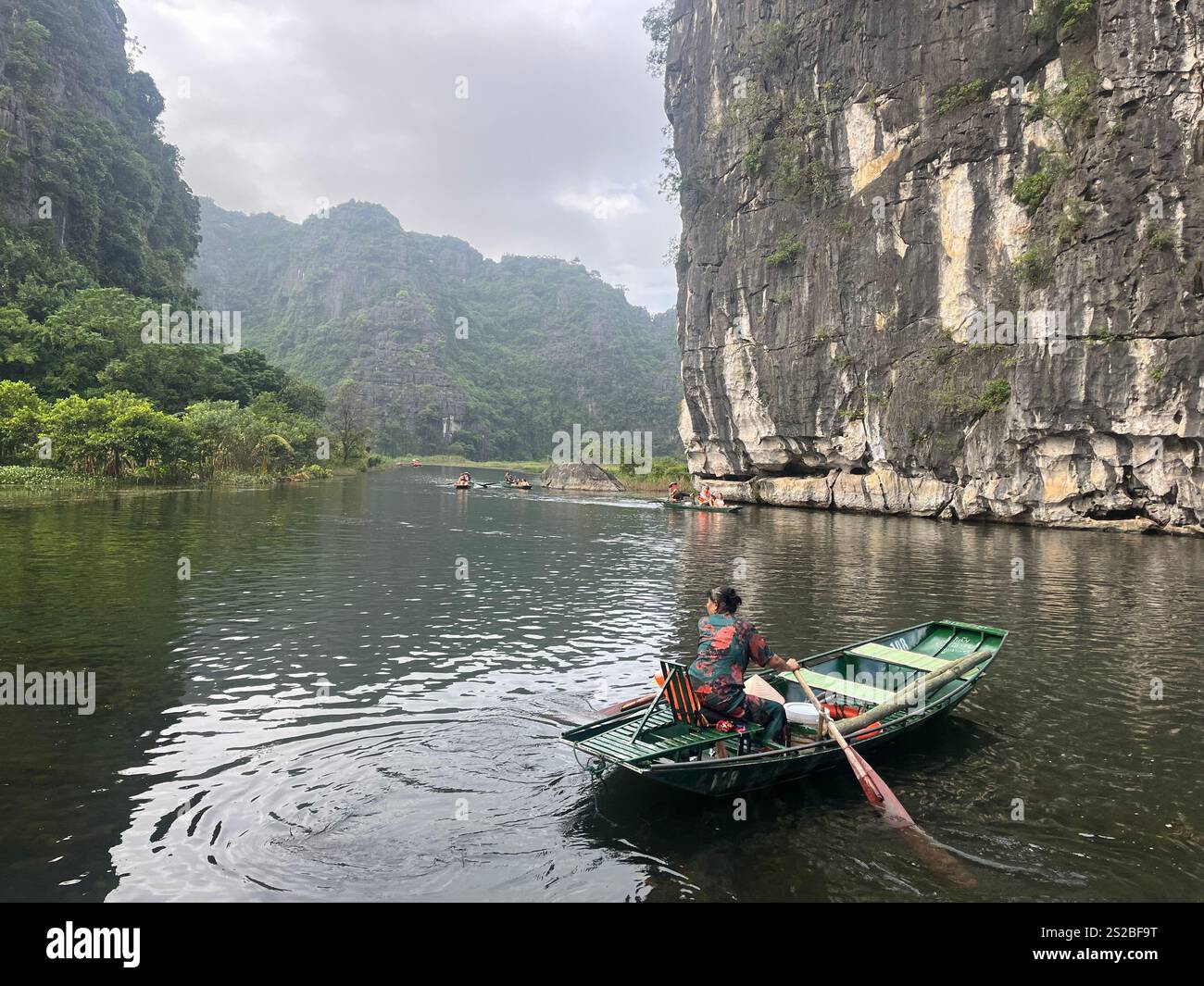 Frau dreht ihr Paddelboot in Tam Coc, Ninh Binh, Vietnam. Das Boot wird in einem nebeligen Tal gepaddelt, mit dramatischen Hügeln auf beiden Seiten. Stockfoto
