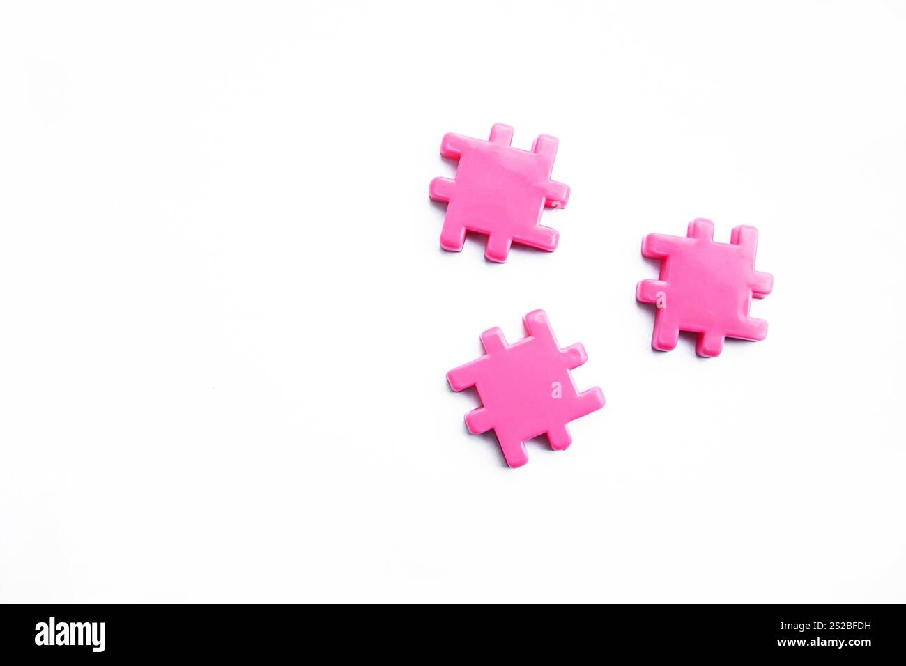 Drei pinkfarbene Puzzleteile, die separat auf einem sauberen weißen Hintergrund platziert werden, zeigen ihre leuchtenden Farben und einzigartigen Formen Stockfoto