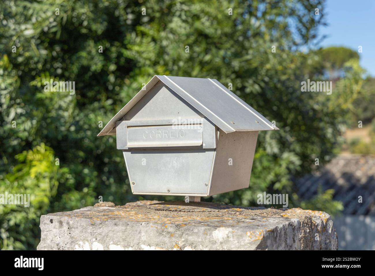 Grauer Aluminiumbriefkasten in Form eines Hauses. Auf der Klappe ist der Text „correio“ eingeprägt. Das portugiesische Wort für Post. Stockfoto