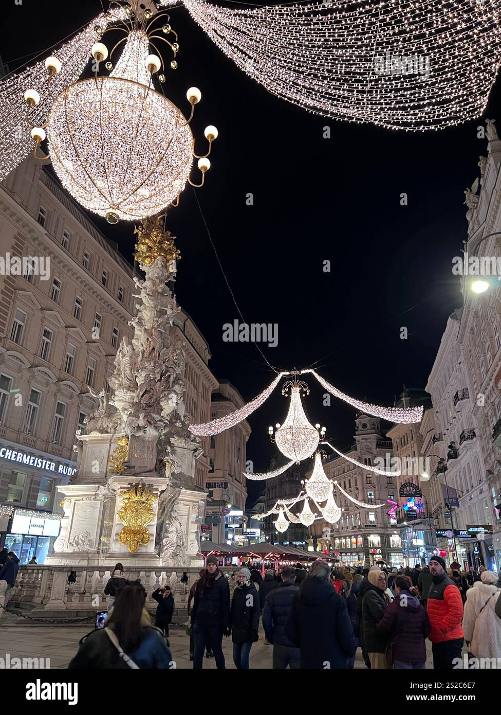 Weihnachtsbeleuchtung in der Fußgängerzone in der Nähe des Stephansplatzes mit dem Denkmal für die Pest-Säule. Die Lichter sind elegante Kronleuchter, die über der Straße hängen. Stockfoto