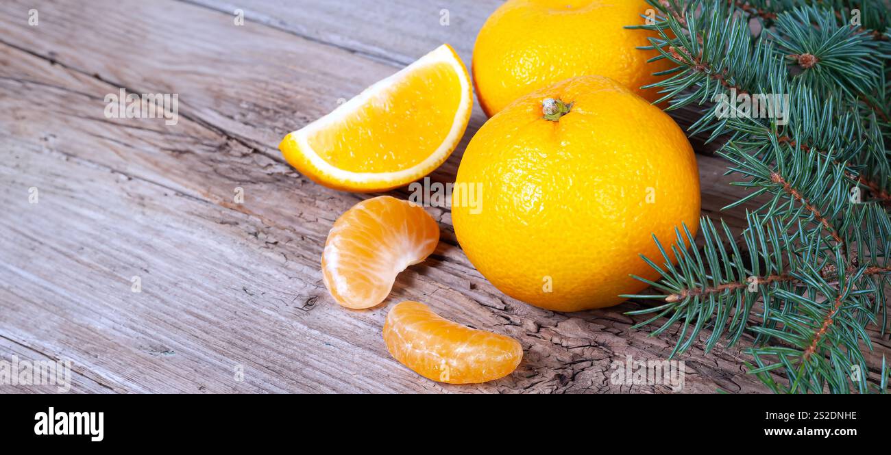 Saftige Orangen- und Mandarinenscheiben sind auf einer verwitterten Holzoberfläche mit Kiefernzweigen angeordnet, die ein frisches, natürliches Ambiente vermitteln. Stockfoto