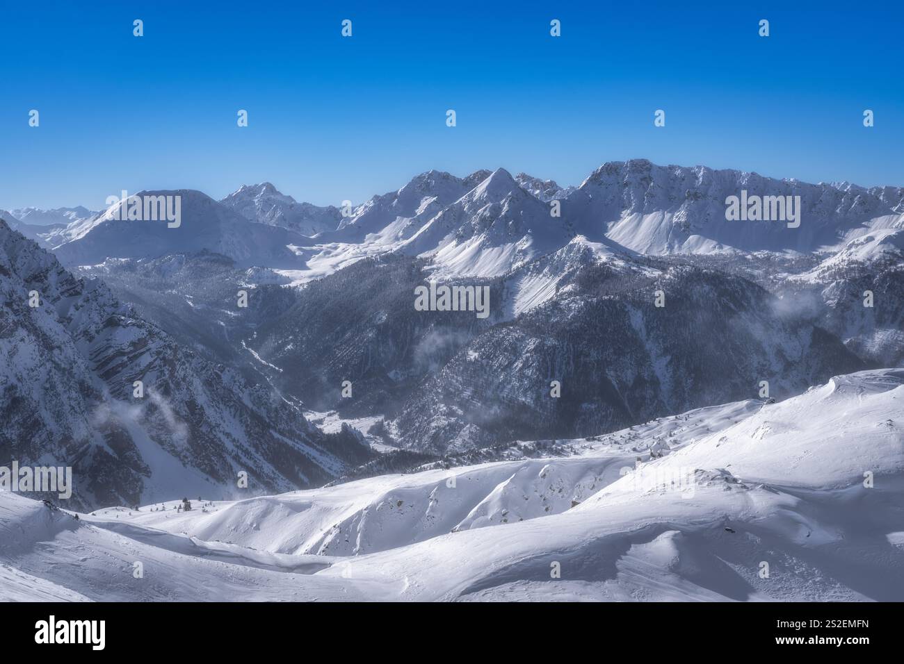 Genießen Sie einen atemberaubenden und atemberaubenden Blick auf die schneebedeckten Berge vor einem strahlend blauen Himmel, der die majestätische Schönheit des Winters zeigt Stockfoto