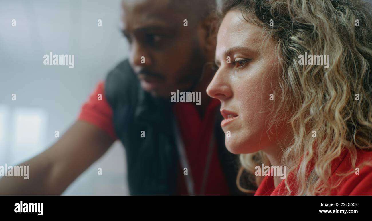 Nahaufnahme zweier verschiedener Postmitarbeiter, die sich unterhalten, E-Commerce-Bestellungen für den Versand vorbereiten, Informationen über Pakete auf dem Computer überprüfen. Arbeiten im Lager des Online-Shops. Stockfoto