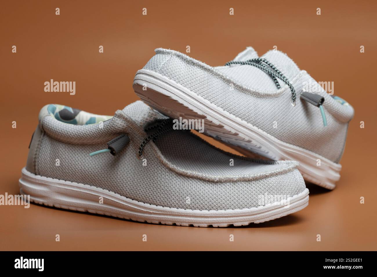 Hellgraue Freizeitschuhe mit schlichtem Design vor warmem, solidem Hintergrund, die ihren Komfort betonen. Stockfoto