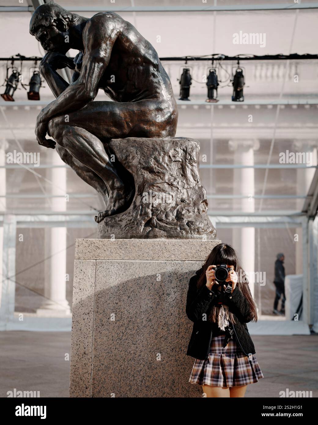 Junge Frau, die unter der Statue des Thinkers steht und einen Fotorock nimmt Stockfoto