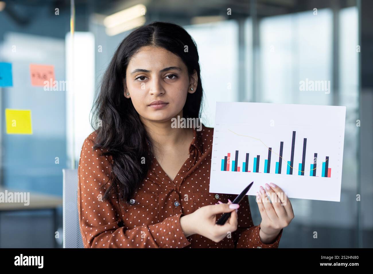 Video-Online-Präsentation, Geschäftsfrau, die in die Webcam blickt, zeigt Berichtsdiagramme mit Einkommen- und Finanzindikatoren in die Kamera, Büroangestellte im Büro am Arbeitsplatz. Stockfoto