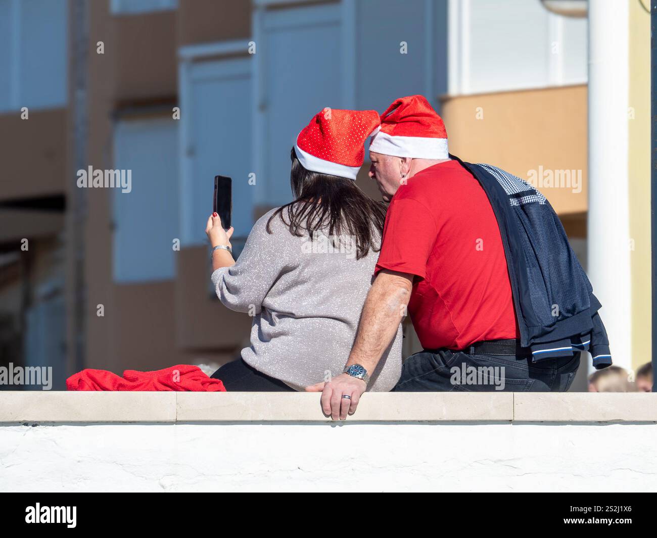 12/25/2024 . Malaga, Spanien. Ein heterosexuelles Paar, das als Weihnachtsmann verkleidet ist und am Rande der Promenade in Malaga sitzt. Stockfoto 12/25/2024 . Malaga, Spanien. Ein heterosexuelles Paar, das als Weihnachtsmann verkleidet ist und am Rande der Promenade in Malaga sitzt. Stockfoto