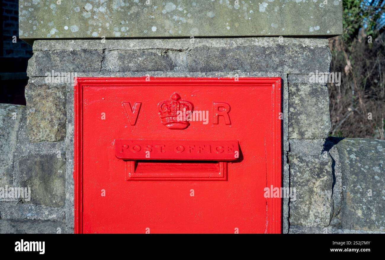 Roter viktorianischer Briefkasten zur Wandmontage vor dem Bahnhof Haworth. Stockfoto