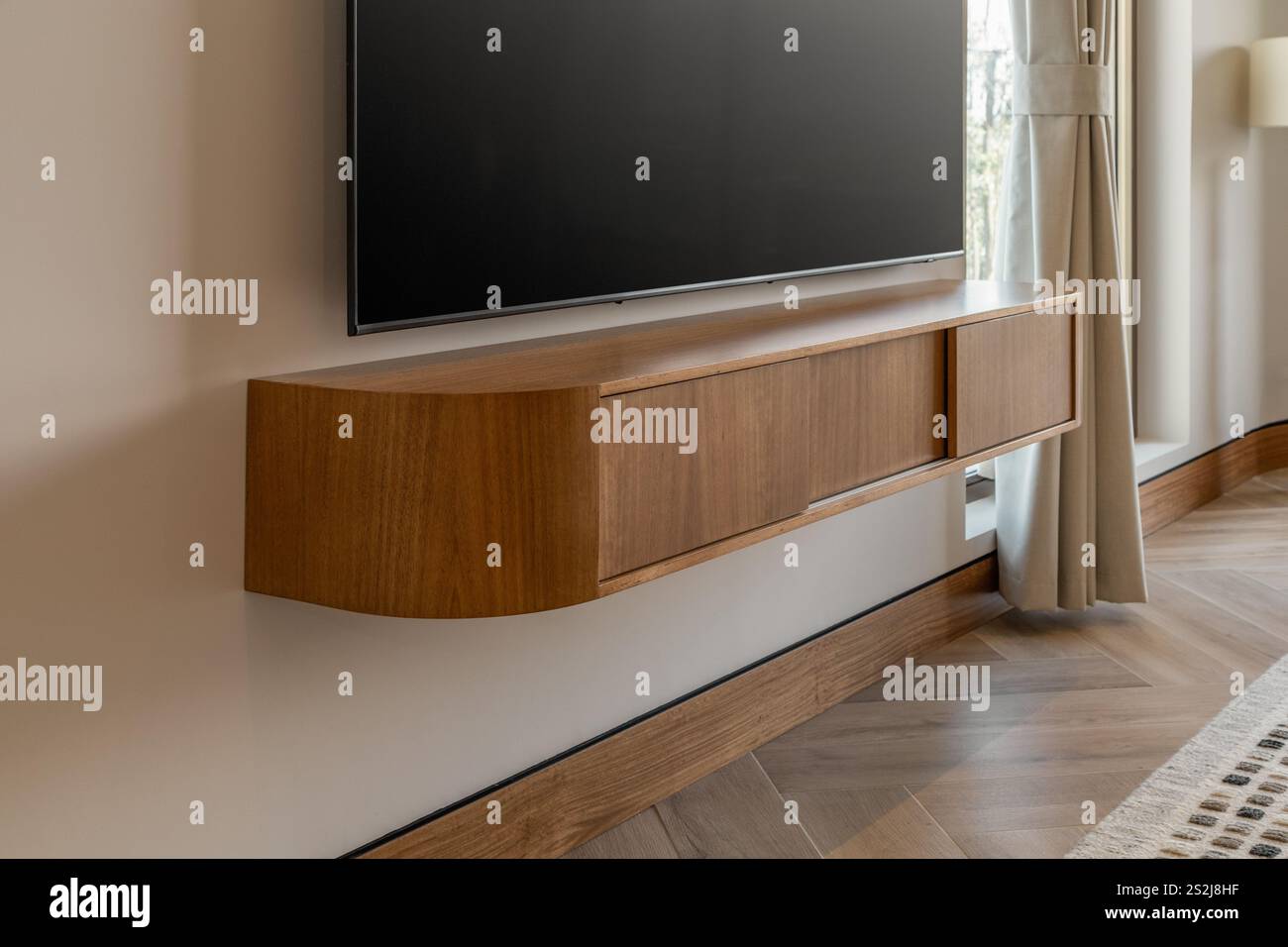 Ein Fernseher auf einer Holzkonsole, der eine moderne, aber warme Atmosphäre schafft. Das schlanke Design der Konsole ergänzt den Fernseher und macht ihn zu einem stilvollen Design Stockfoto