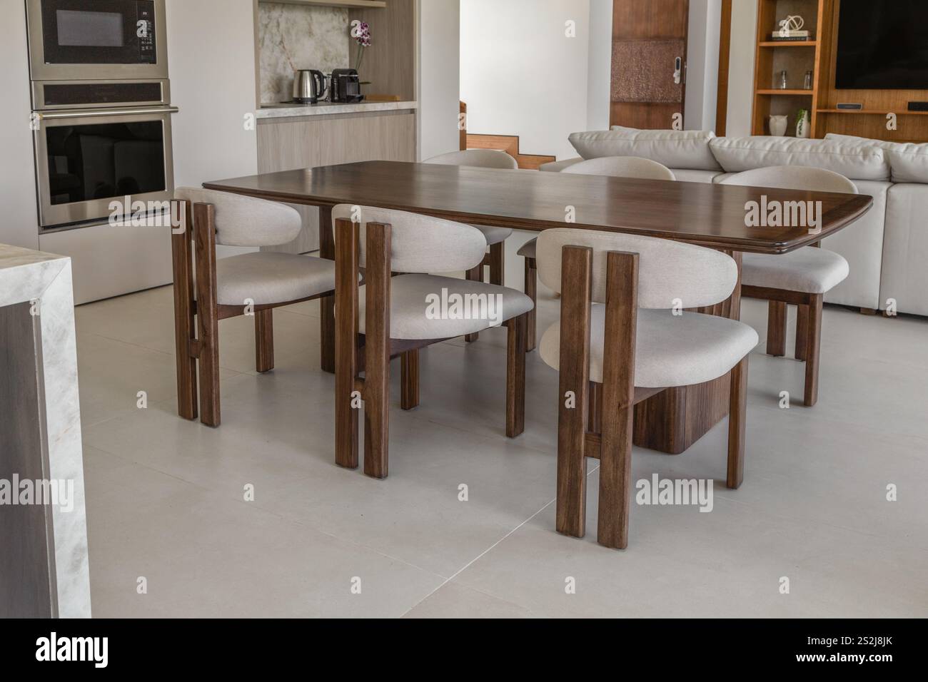 Ein elegantes Esstisch mit Holzstühlen und gepolsterten Sitzen sowie einem eleganten Esstisch aus Glas. Perfekt für moderne Esszimmer Stockfoto