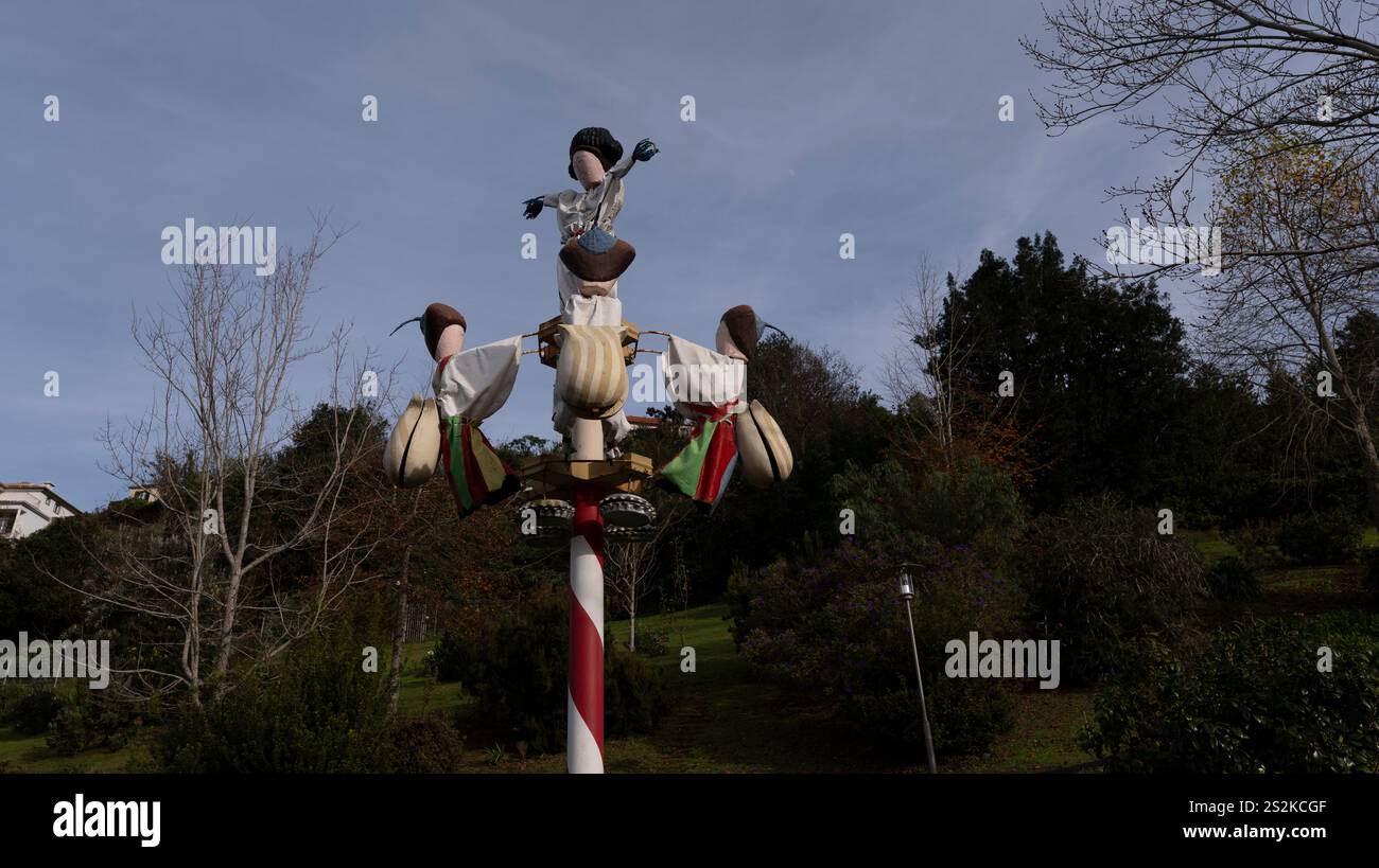 Eine skurrile Skulptur im Freien mit drei Figuren in dynamischen Posen auf einem gestreiften Stab, vor einem natürlichen Park mit Bäumen und grünem Hintergrund Stockfoto