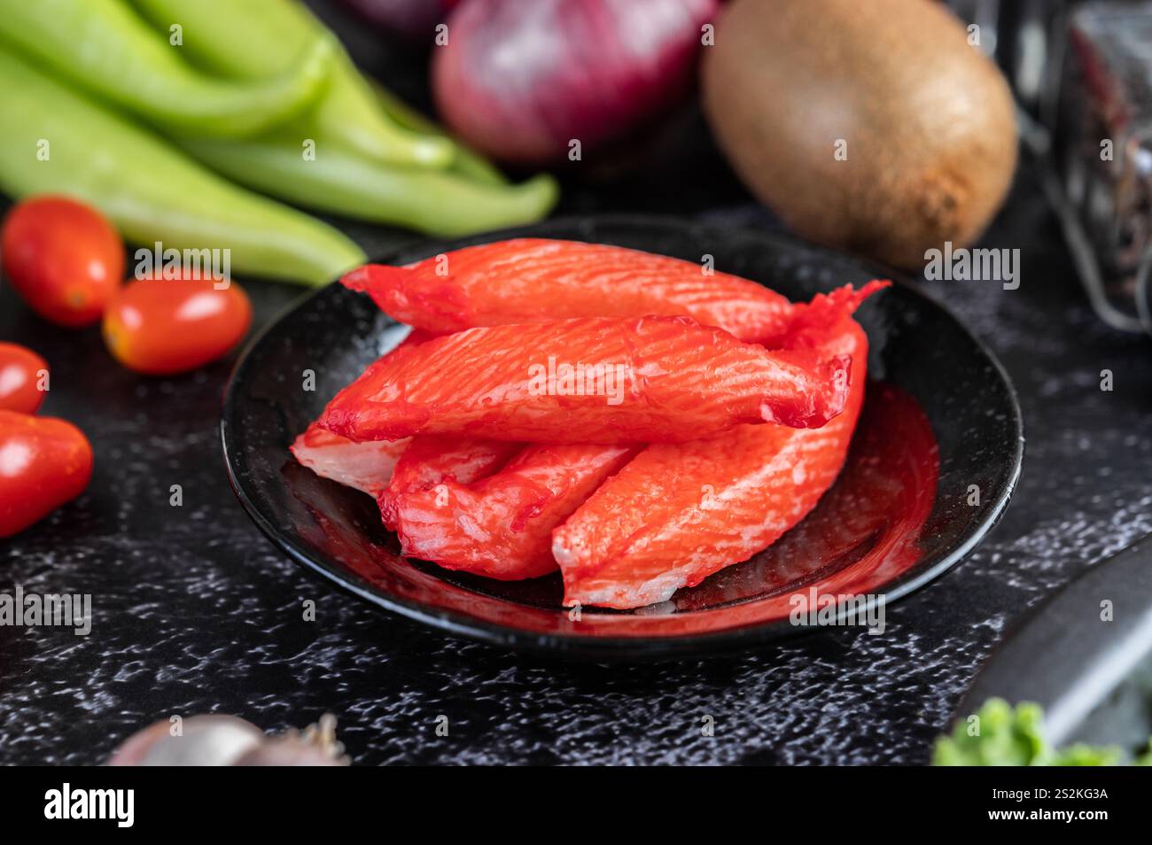 Krabbenstab auf einen schwarzen Teller mit rohen Lachs, Tomaten, Kiwi, Schalotten und süßen Paprika auf dem schwarzen Zementboden. Stockfoto