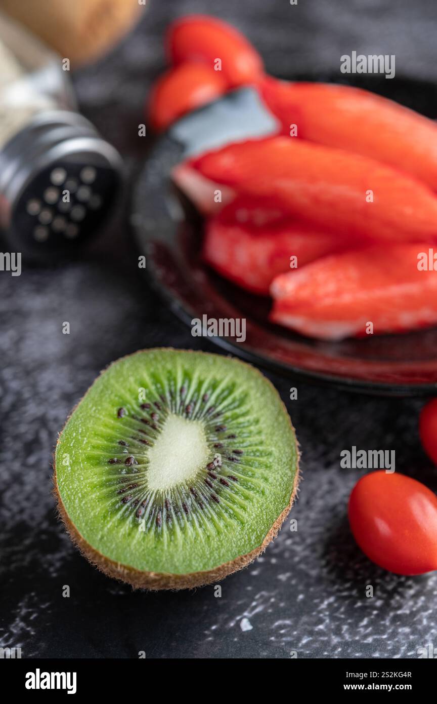 Krabbenstab auf einen schwarzen Teller mit rohen Lachs, Tomaten, Kiwi, Schalotten und süßen Paprika auf dem schwarzen Zementboden. Fokus Kiwi. Stockfoto