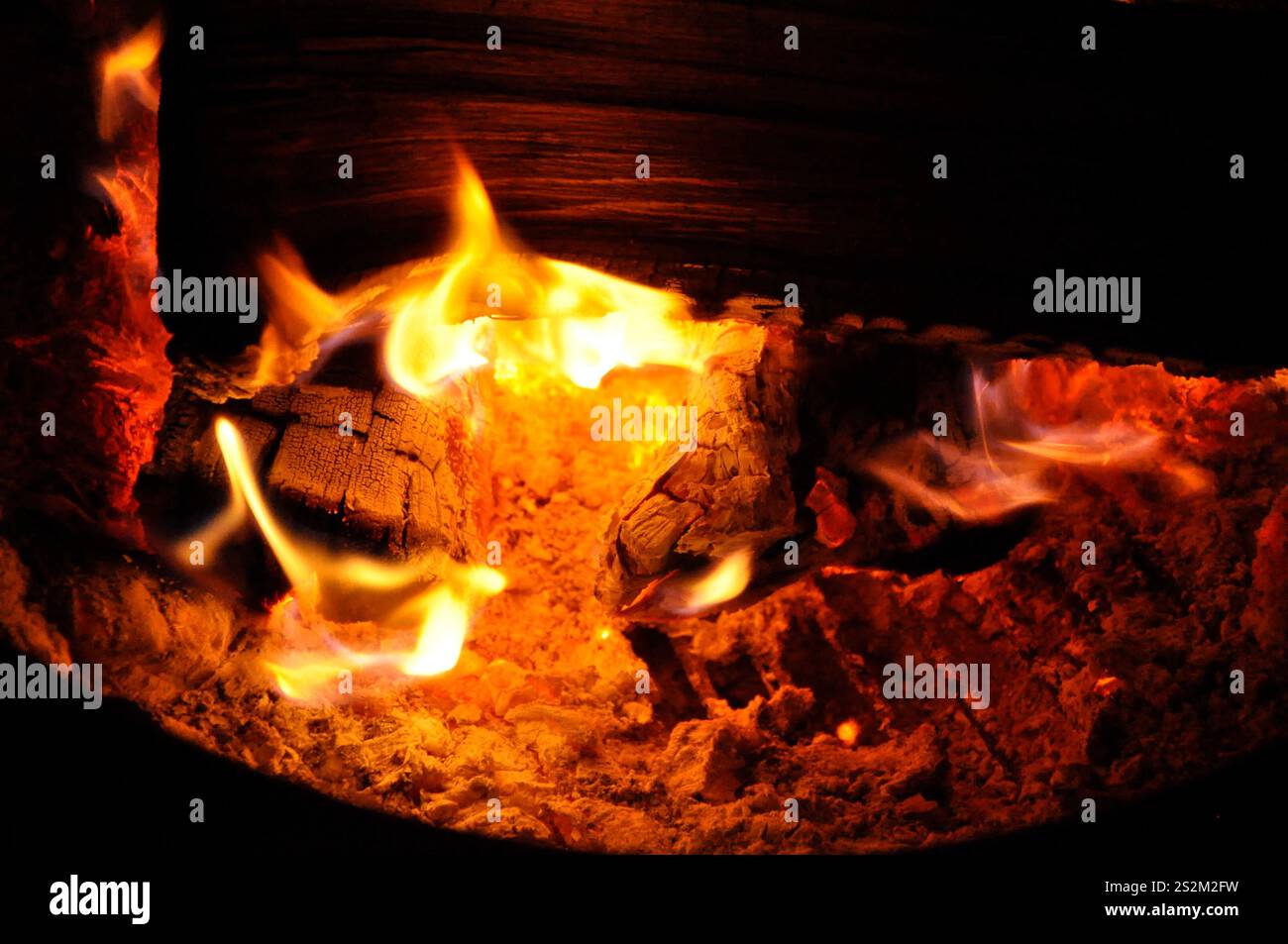 Flammen tanzen zwischen der glühenden Glut der Holzscheite eines Grillfeuers. Stockfoto Flammen tanzen zwischen der glühenden Glut der Holzscheite eines Grillfeuers. Stockfoto