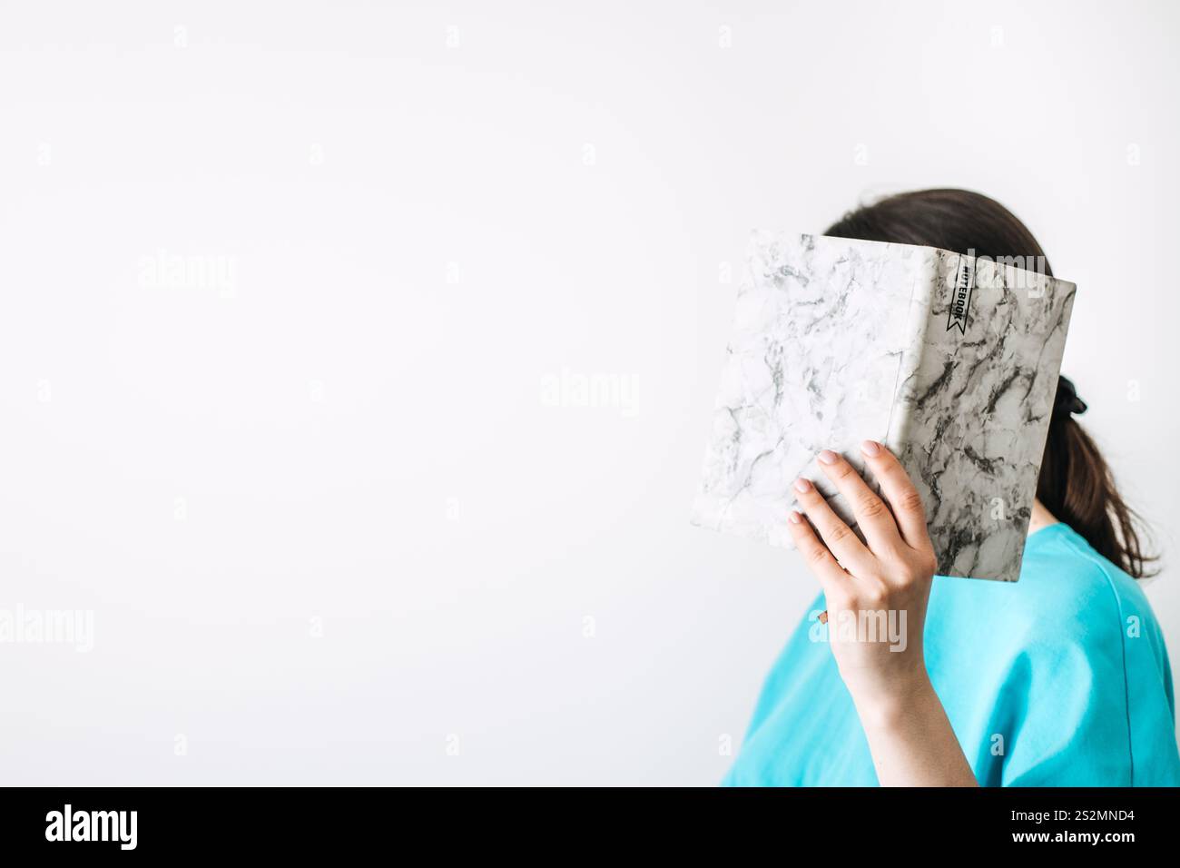 Lächelnde Frau mit Notizbüchern in minimalistischer Umgebung. Selbstreflexion durch Schreiben, kreativen Ausdruck und persönliches Wachstum mit modernem Tagebuch Stockfoto