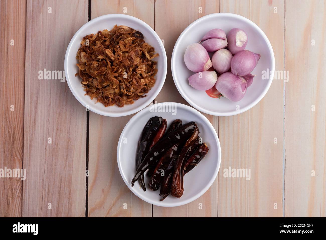 Zwiebeln, getrocknete Chilis und rote Zwiebeln auf einem weißen Teller auf einem Holzboden anbraten. Draufsicht Stockfoto