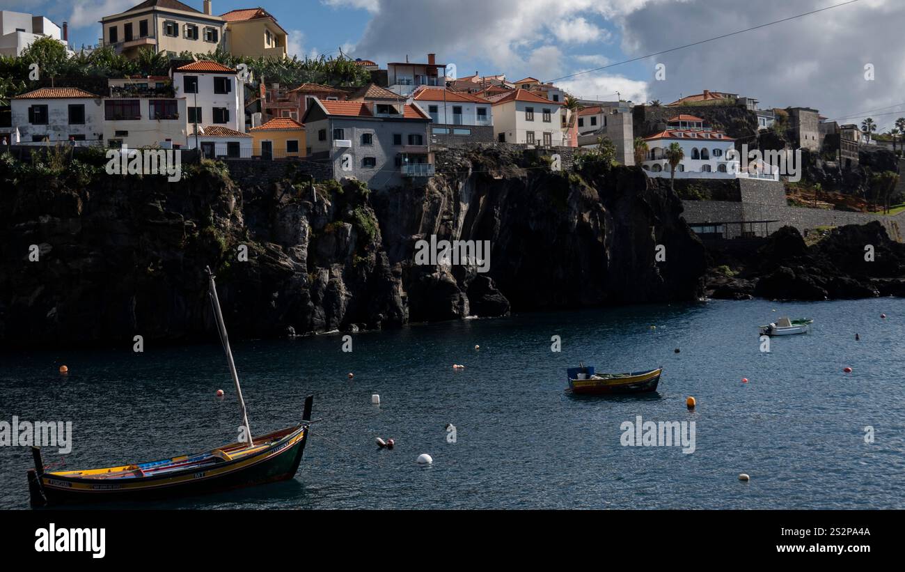 Ein Küstendorf mit bunten Häusern auf einer felsigen Klippe mit Blick auf das ruhige blaue Wasser. Traditionelle Holzboote schweben im Vordergrund und fügen hinzu Stockfoto