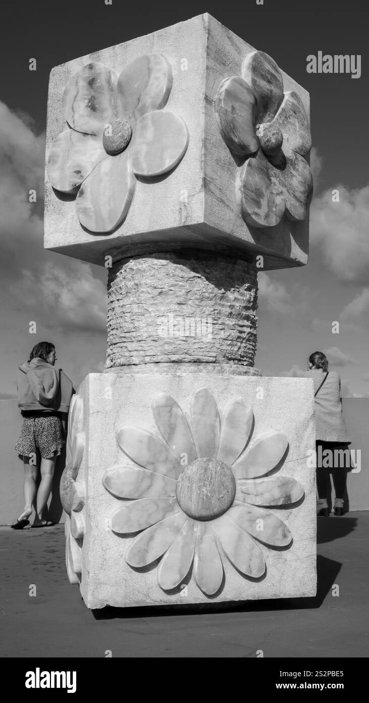 Ein Schwarzweiß-Foto einer großen dekorativen Skulptur mit Blumenmotiven, in der zwei Personen vor einem bewölkten Himmel stehen. Stockfoto