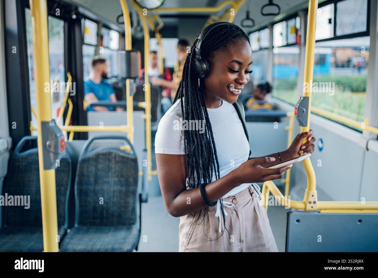 Porträt einer afroamerikanerin, die Ohrhörer trägt und ein Smartphone benutzt, während sie im Bus fährt. Schwarze Frau mit Zöpfen, die in den sozialen Medien auftaucht Stockfoto