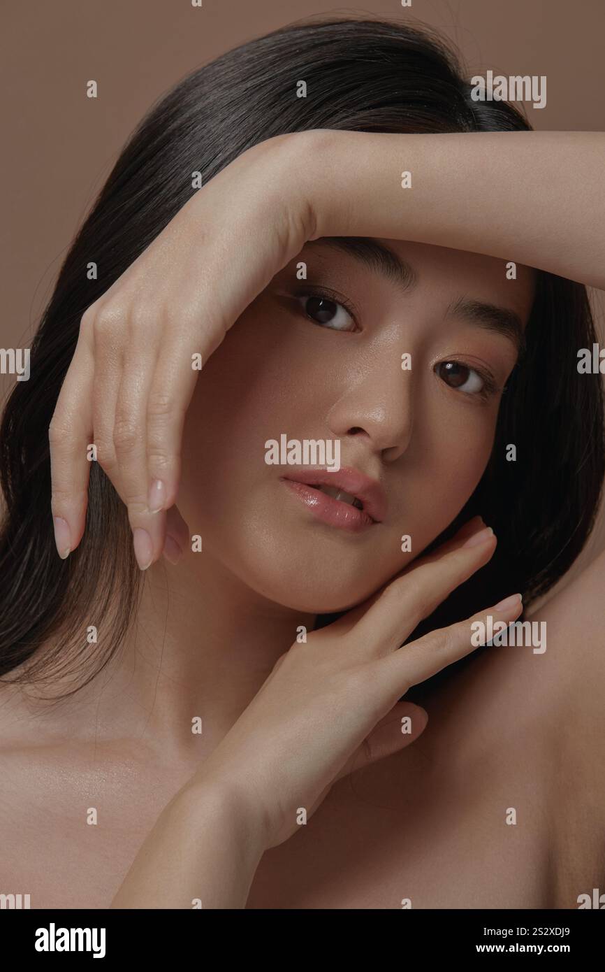 Porträt einer asiatischen Frau mit einer sauberen gesunden Haut und schönen Händen nahe ihrem Gesicht über beigem Hintergrund, vertikales Nahaufnahme Foto Stockfoto
