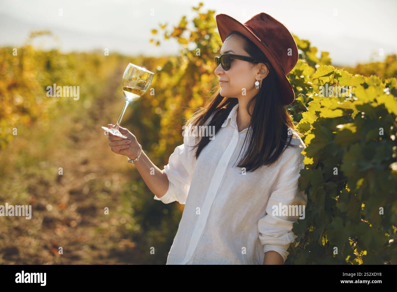 Frau mit Hut und Sonnenbrille, die ein Glas Wein hält Stockfoto