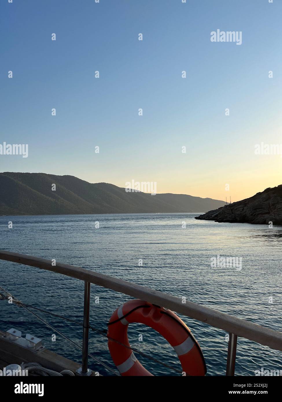 Eine wunderschöne vertikale Aufnahme einer Yacht bei Sonnenuntergang auf dem Meer mit Bergen im Hintergrund. Fantastische Yachtfahrt in Bodrum, Türkei. Stockfoto