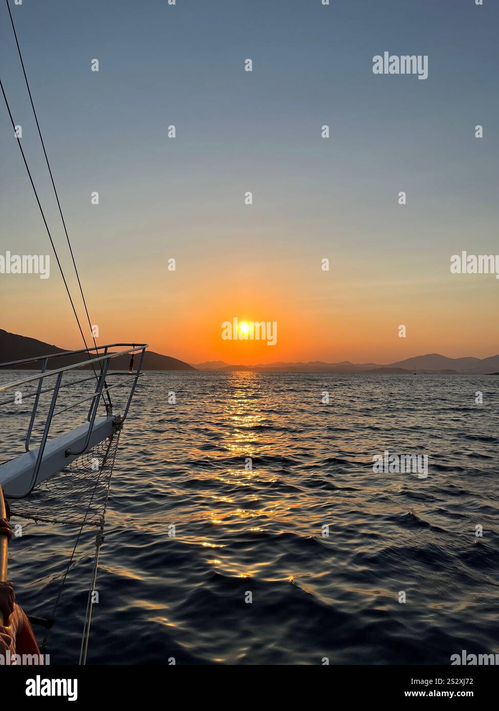 Eine wunderschöne vertikale Aufnahme eines orangen Sonnenuntergangs auf dem Meer mit Bergen im Hintergrund. Fantastische Yachtfahrt in Bodrum, Türkei. Stockfoto